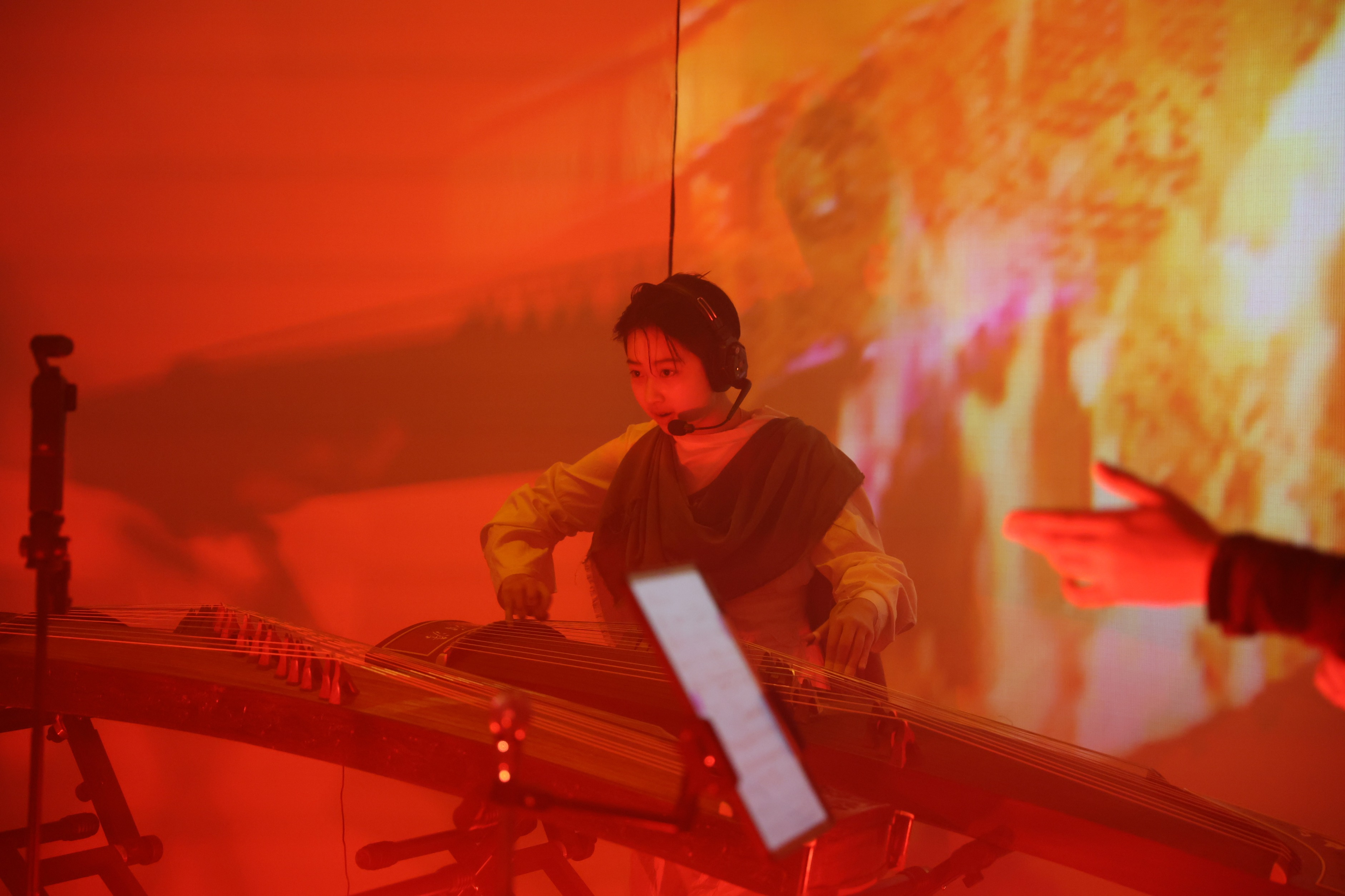 QiQi performing original guzheng music in Echoes of the Earth, with colourful projections and theatrical lighting.